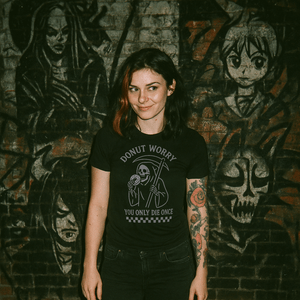 Person wearing a black t-shirt with graphic design in front of a dark wall with artwork
