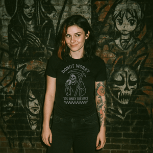 Person wearing a black t-shirt with graphic design in front of a brick wall with artwork.