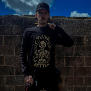 Person wearing a black sweatshirt with a skeleton design and text, standing against a brick wall.