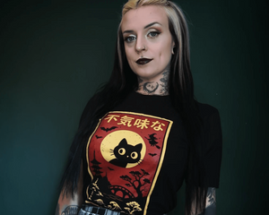 Person wearing a black t-shirt with a cat graphic and text, standing against a dark background